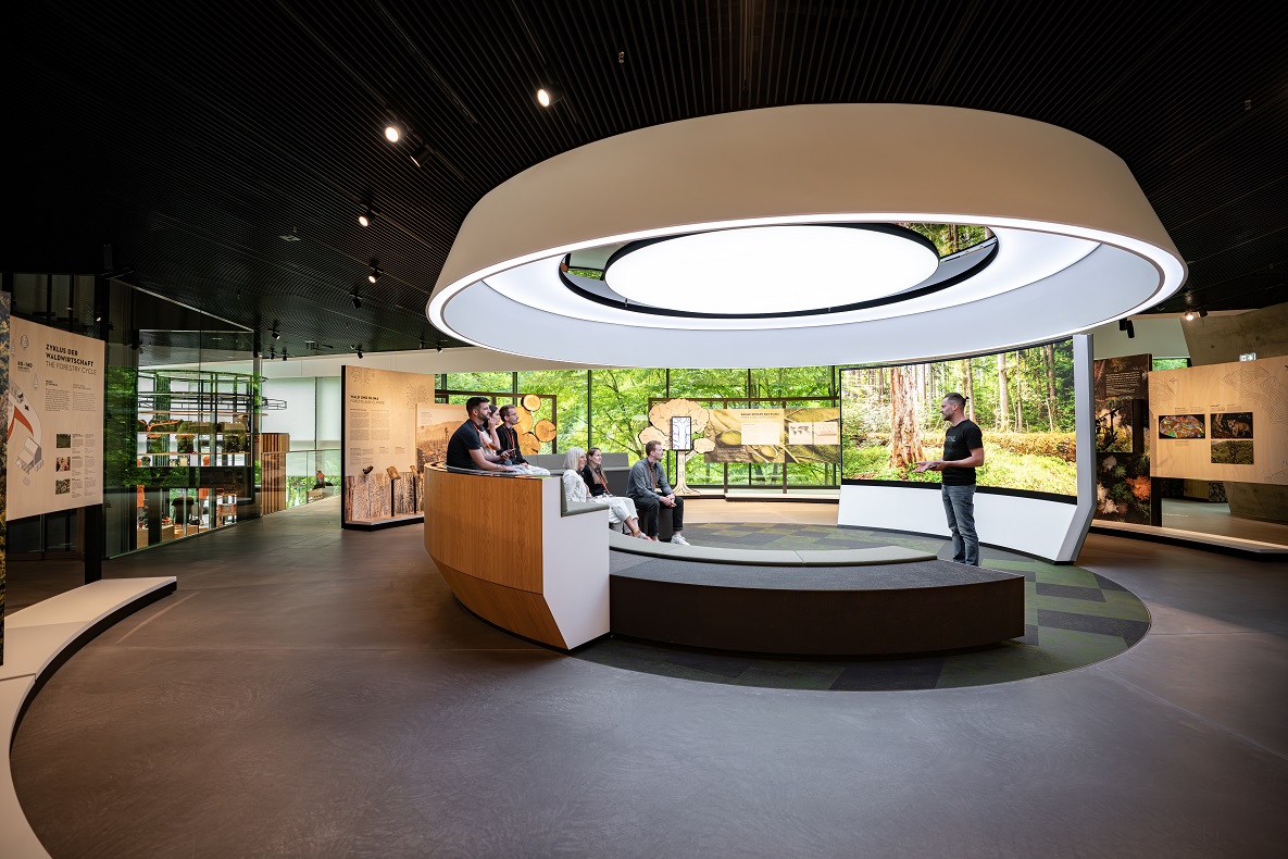 A modern presentation room in the STIHL Brand World with visitors, a large light circle, and nature-themed motifs in the background.