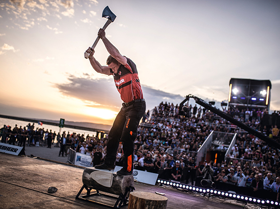 A TIMBERSPORTS® athlete stands on a sturdy log and swings an axe with power.