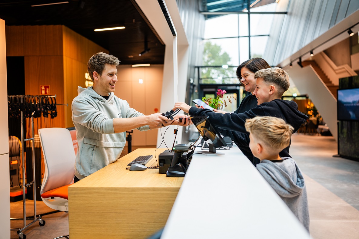 Ein Mitarbeiter der STIHL Markenwelt übergibt Besuchern Headsets.